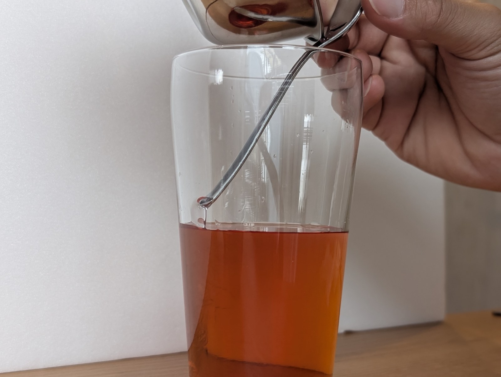 グラスの内がわに立てかけたスプーンの背を伝わせて、砂糖水を注いでいるところ