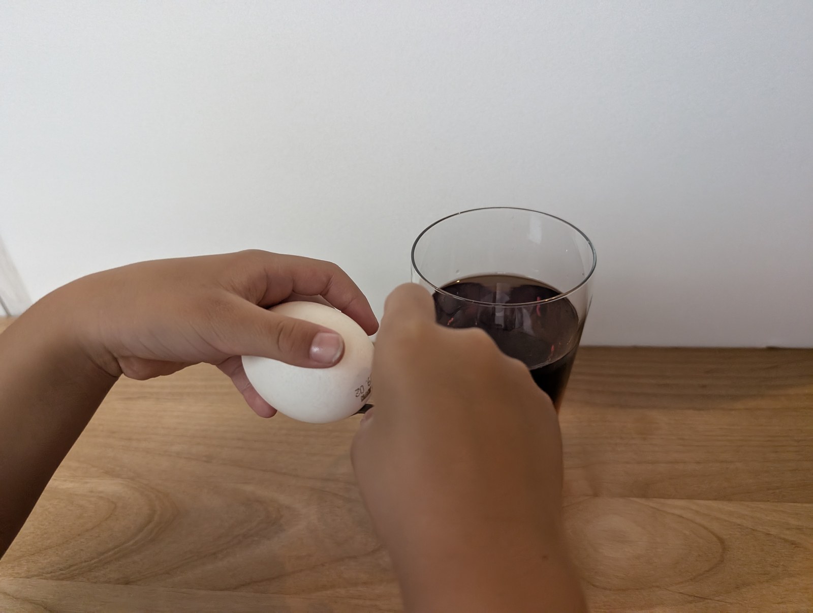 子どもが生卵を手に持ち、グラスの横で構えている
