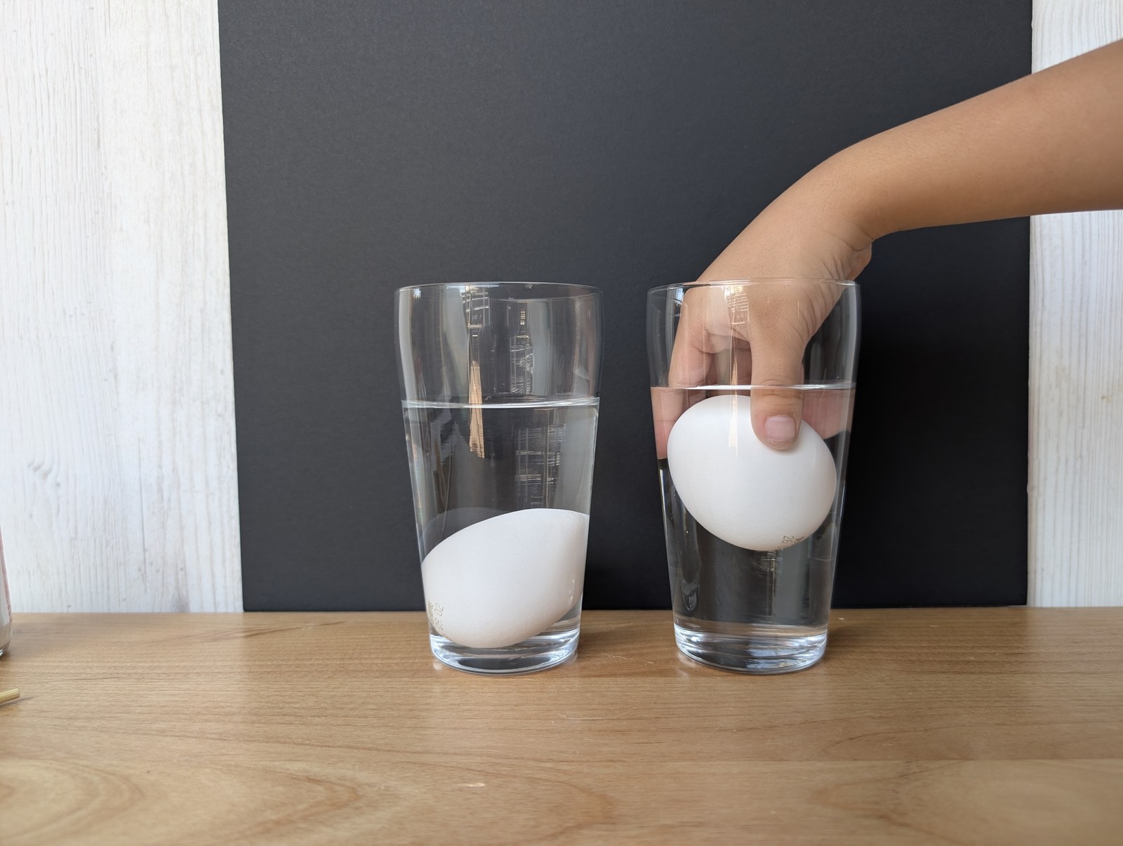 子どもの手が、卵をコップの水にそっと入れているところ
