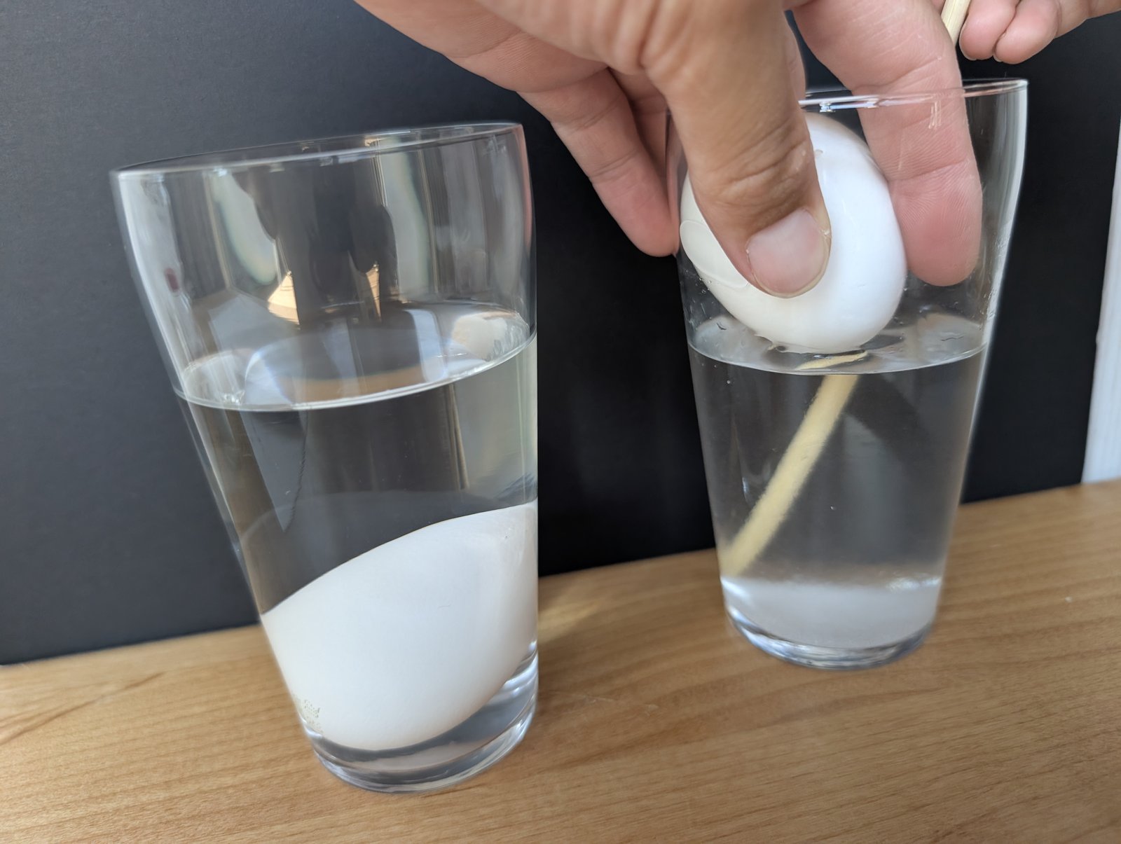 卵を指でつまんで持ち上げながら、菜箸でコップの中を混ぜているところ
